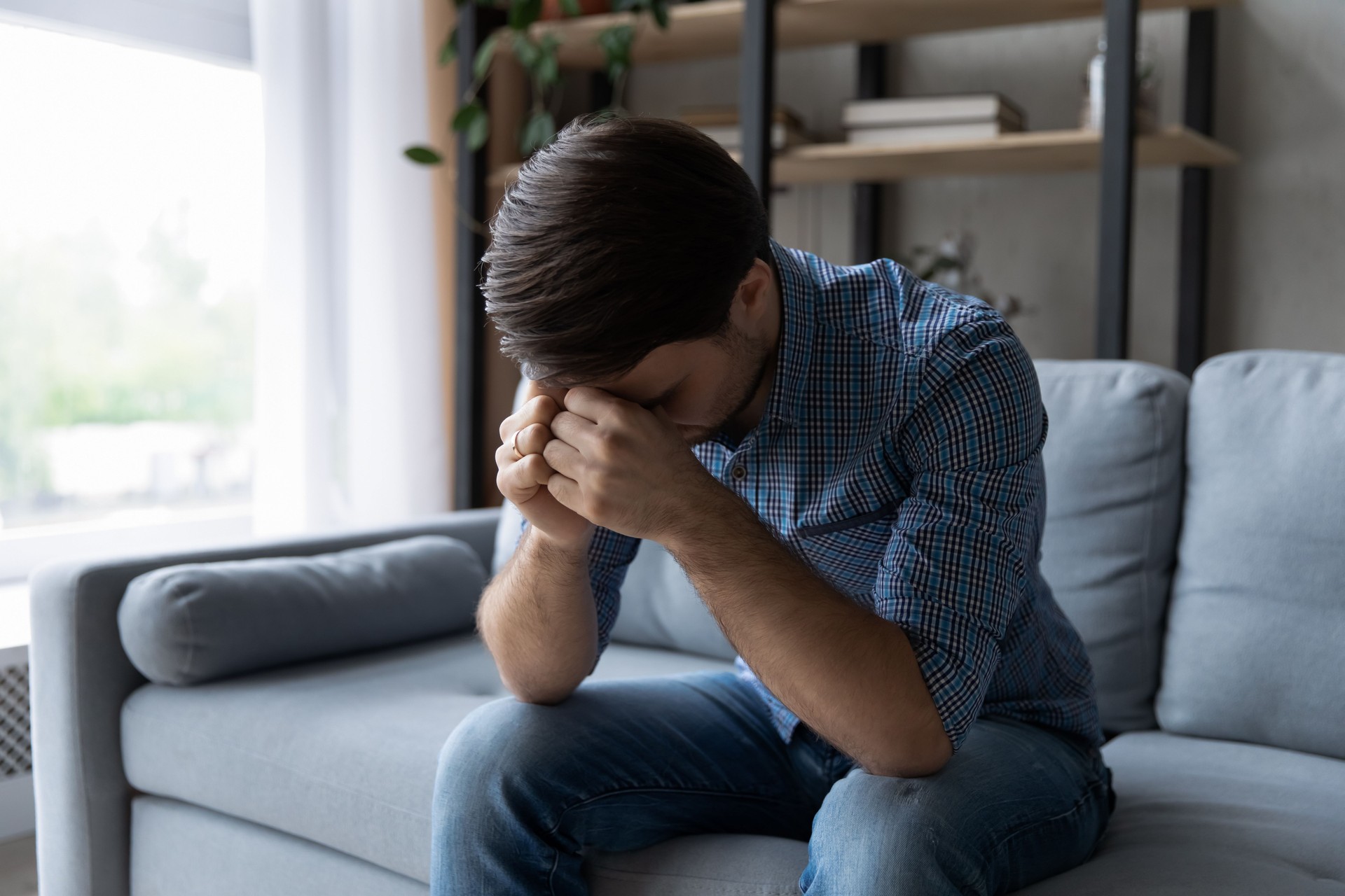 Hombre triste y deprimido sentado en el sofá con la cabeza gacha