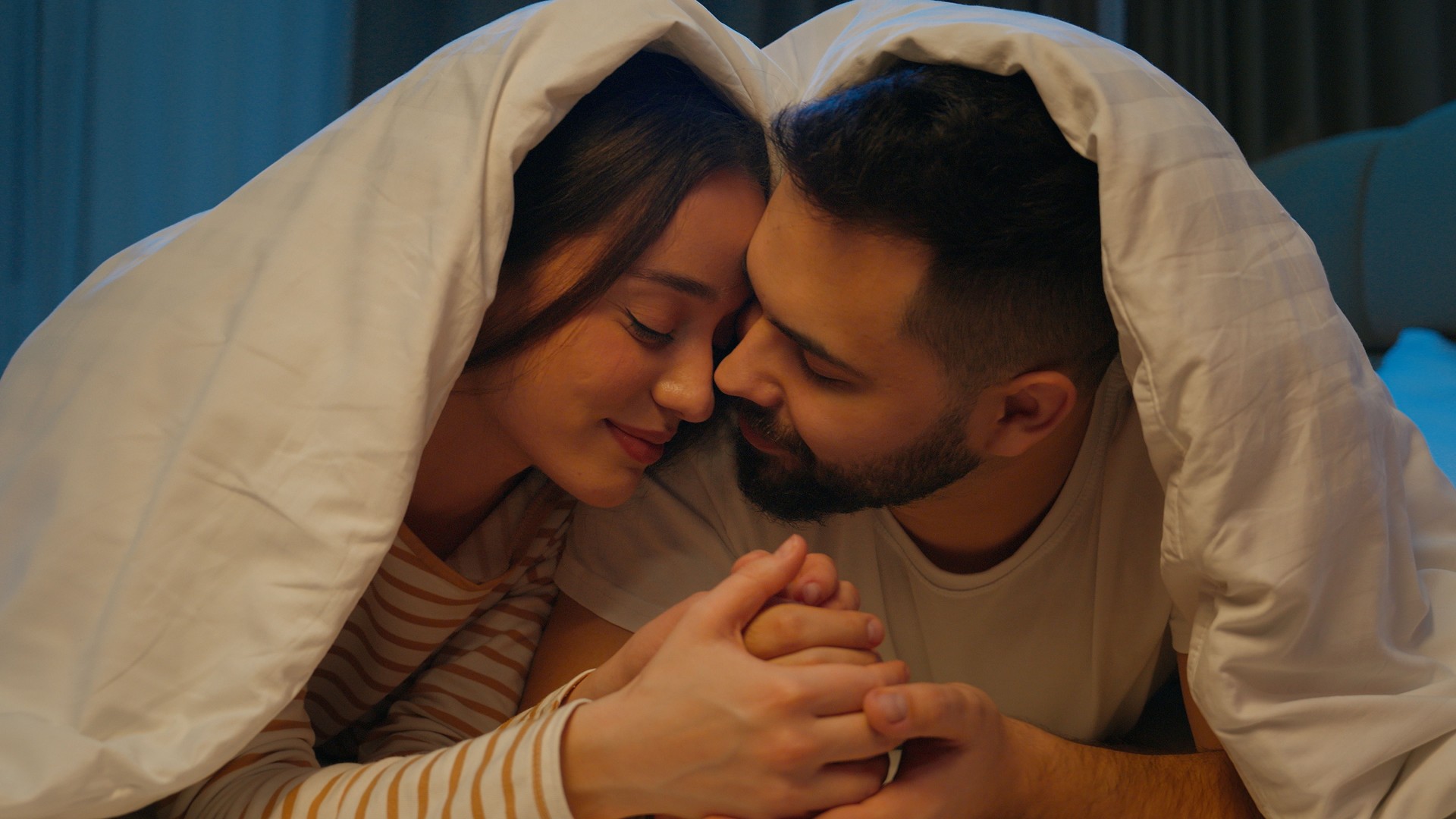 Hombre mujer novio novia beso en la mejilla frotar narices pareja amor esposo esposa mujer masculino armonía sentimientos cariño luna de miel romance unión amado cariñosa ternura edredón cama dormitorio casa