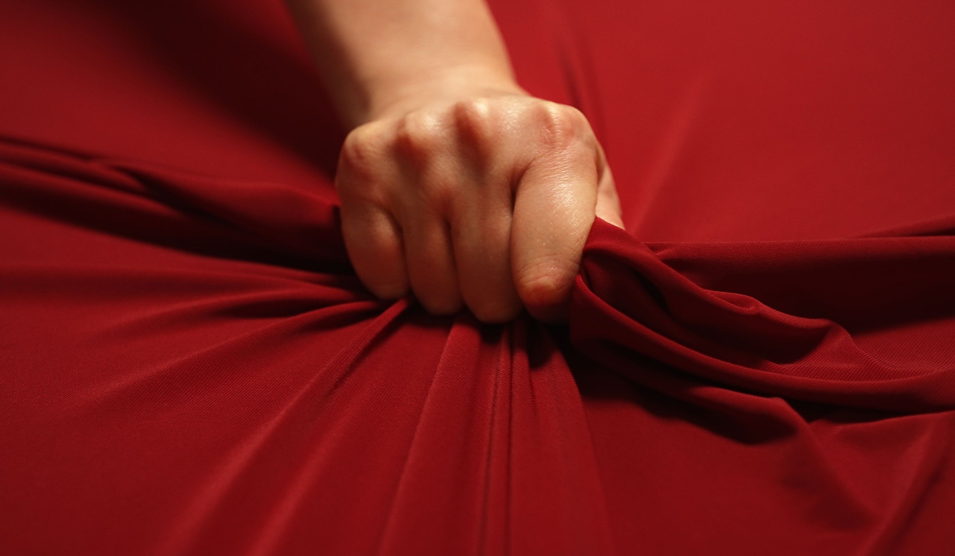 La mano de la mujer aprieta apasionadamente la sábana roja. Concepto de amor.